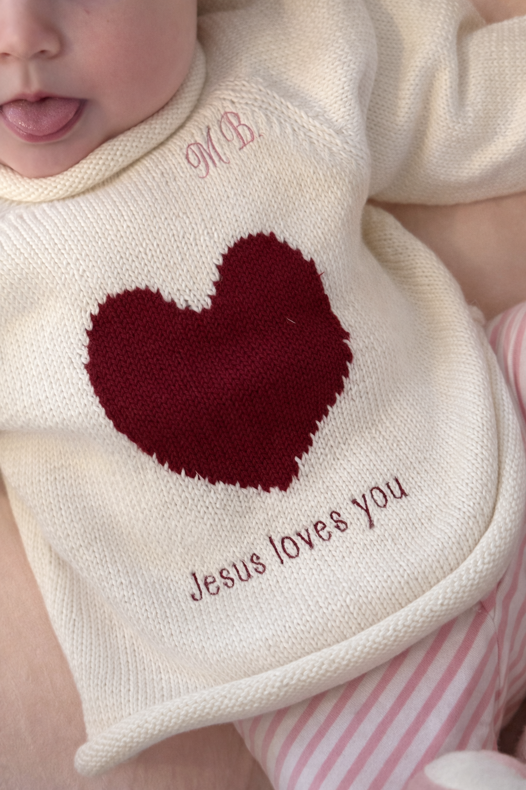 Baby sweater with red heart and 'Jesus loves you' text on a white background