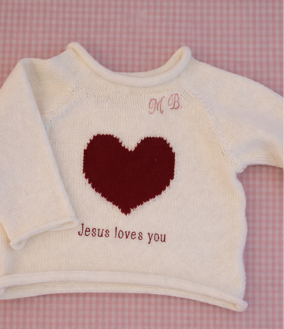 White sweater with a red heart and 'Jesus loves you' text on a pink checkered background